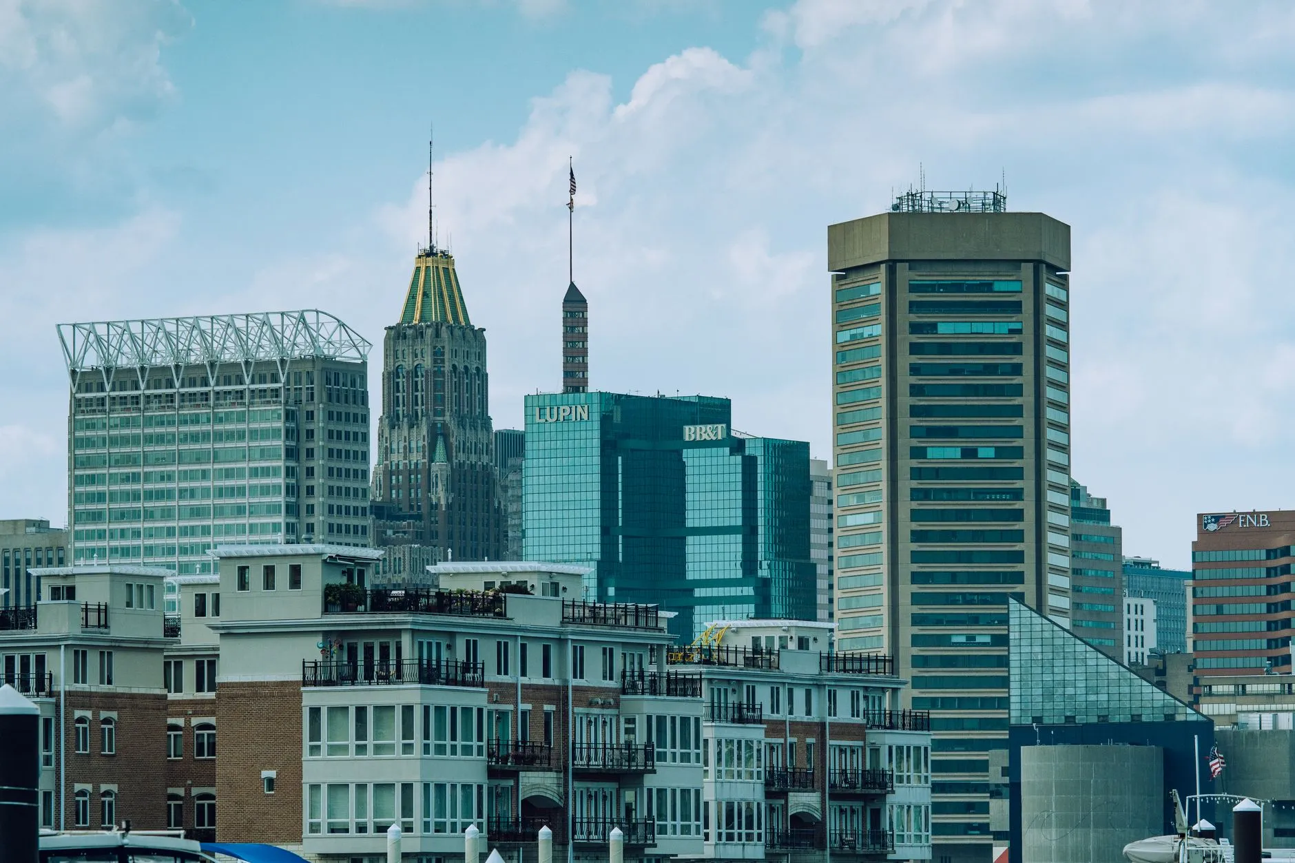 Baltimore's Inner Harbor skyline on a bright day, with the gold-topped Art Deco crown of the Bank of America Building behind the waterfront rowhouses.