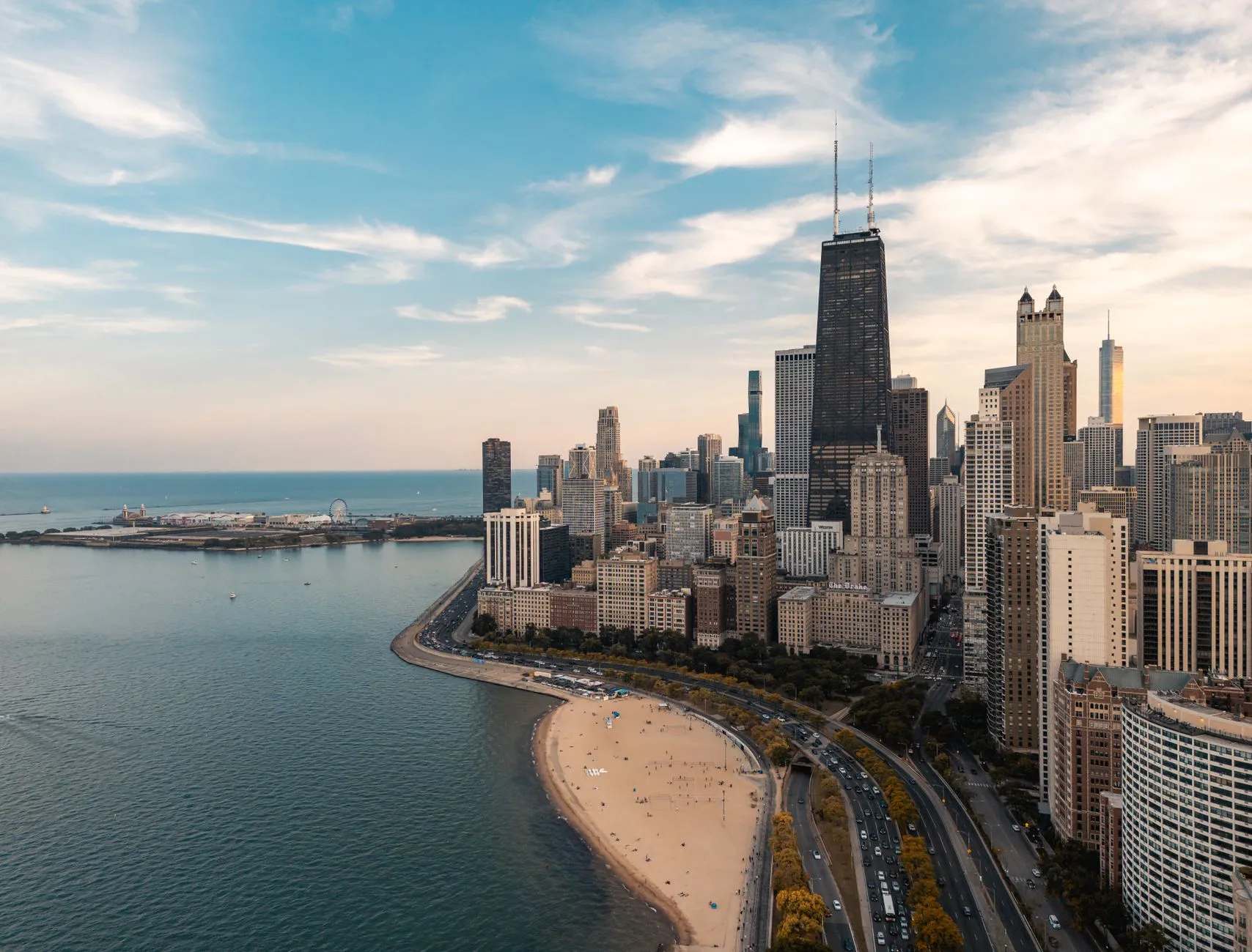 The Chicago lakefront seen from above, with the dark tapered tower of 875 North Michigan Avenue rising over North Avenue Beach and Navy Pier out on Lake Michigan.