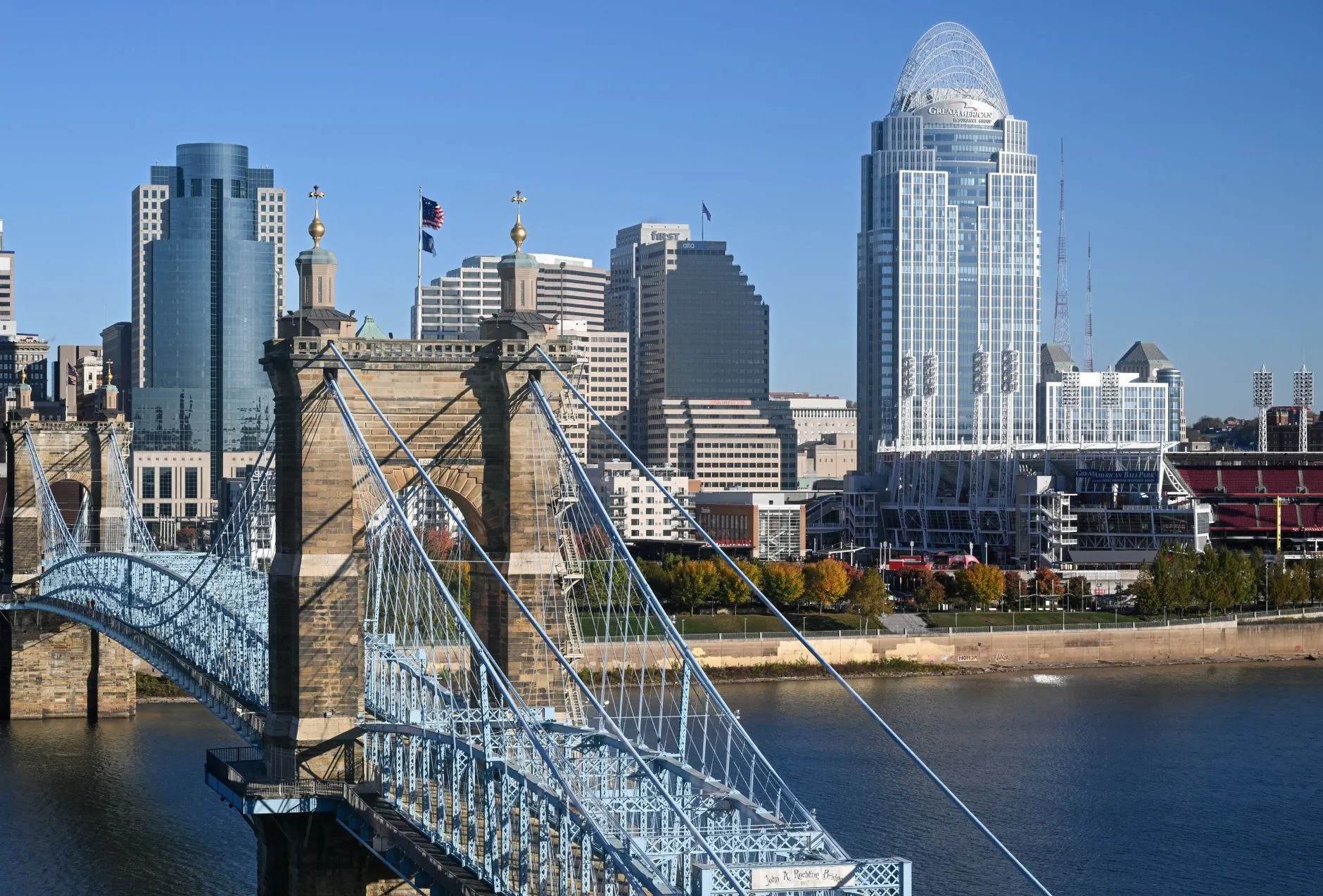 The pale blue John A. Roebling Suspension Bridge crossing the Ohio River, with the Cincinnati skyline and the crowned Great American Tower behind it.