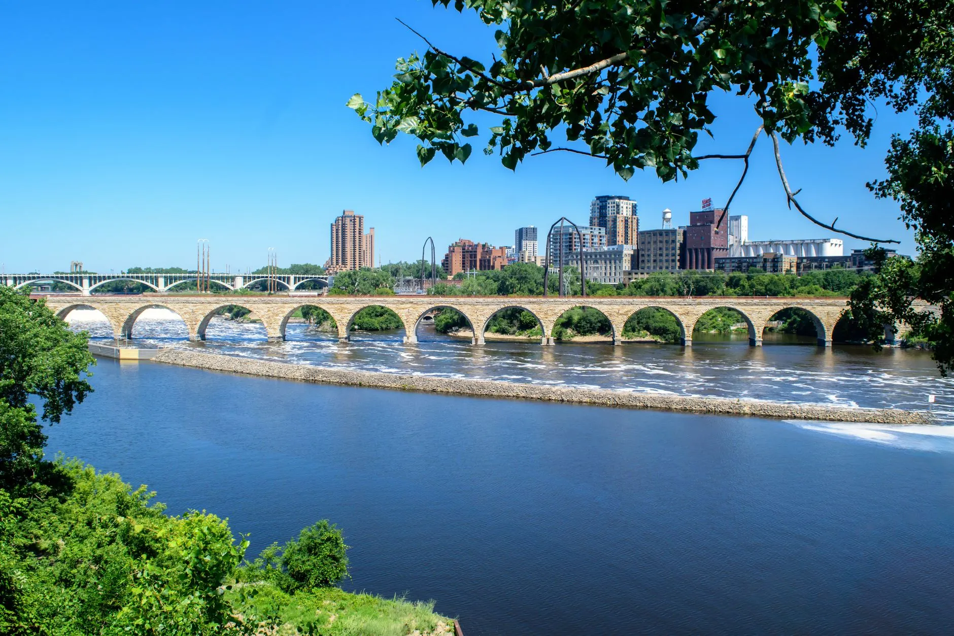 The Stone Arch Bridge curving across the Mississippi River below St. Anthony Falls, with the Minneapolis mill district behind it
