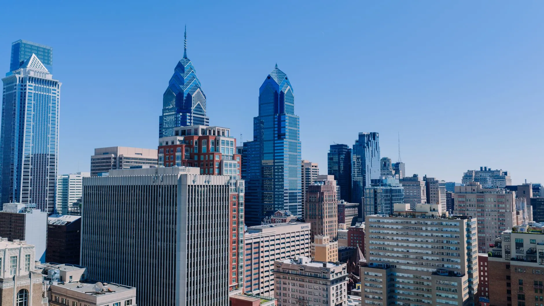 The Center City Philadelphia skyline on a clear day, with the blue chevron crowns of One and Two Liberty Place standing above the surrounding rooftops.