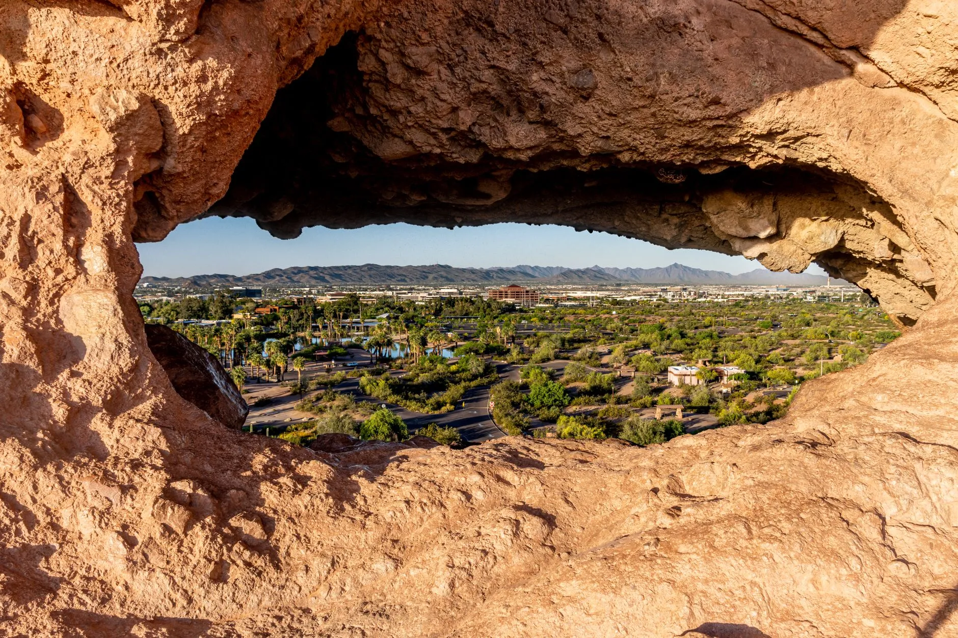 The view out through Hole in the Rock in Phoenix's Papago Park, the eroded sandstone framing the park's palm-lined lagoons and the desert mountains beyond.