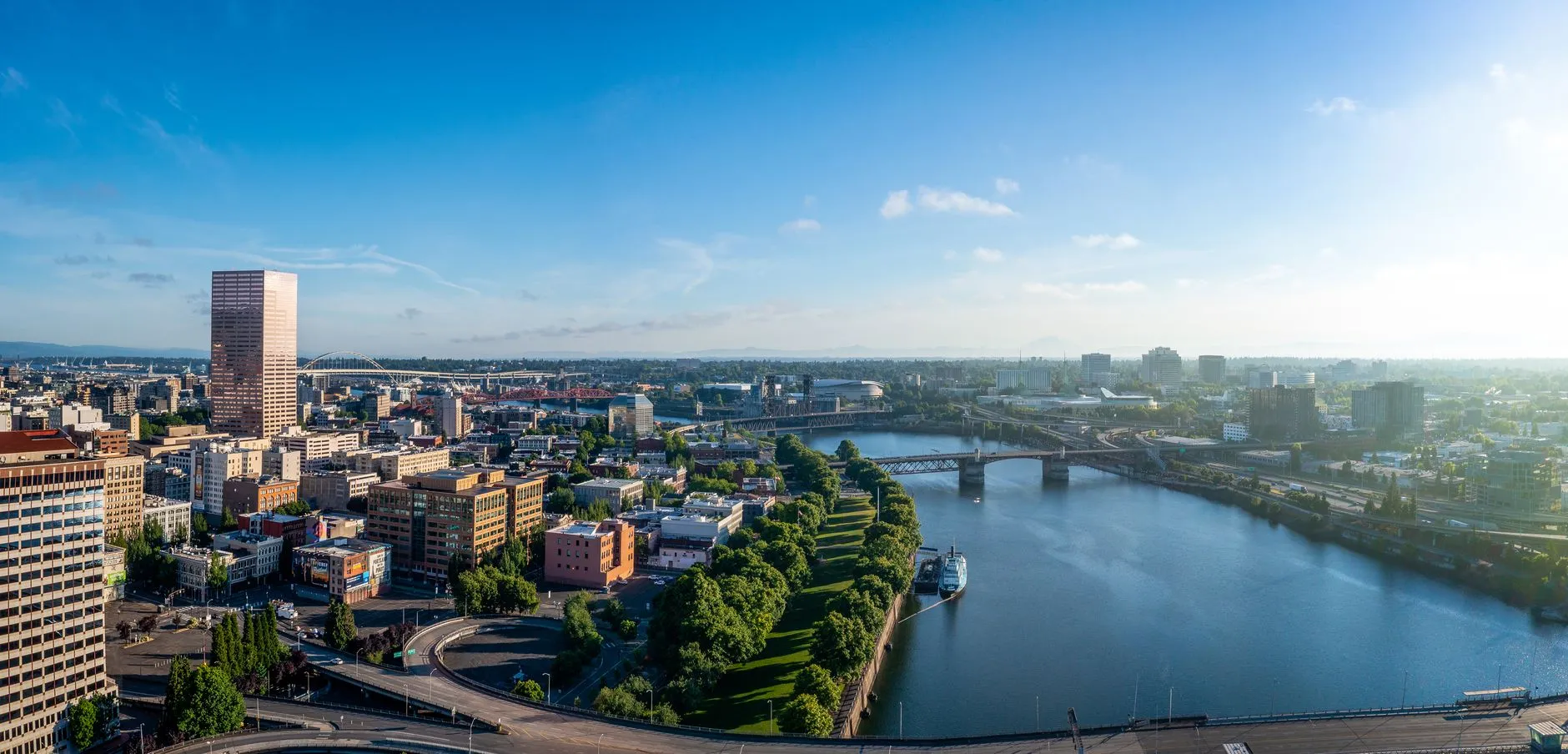 Portland from above on a clear morning, with the rose-coloured US Bancorp Tower over downtown and the Willamette River curving past a run of the city's bridges.