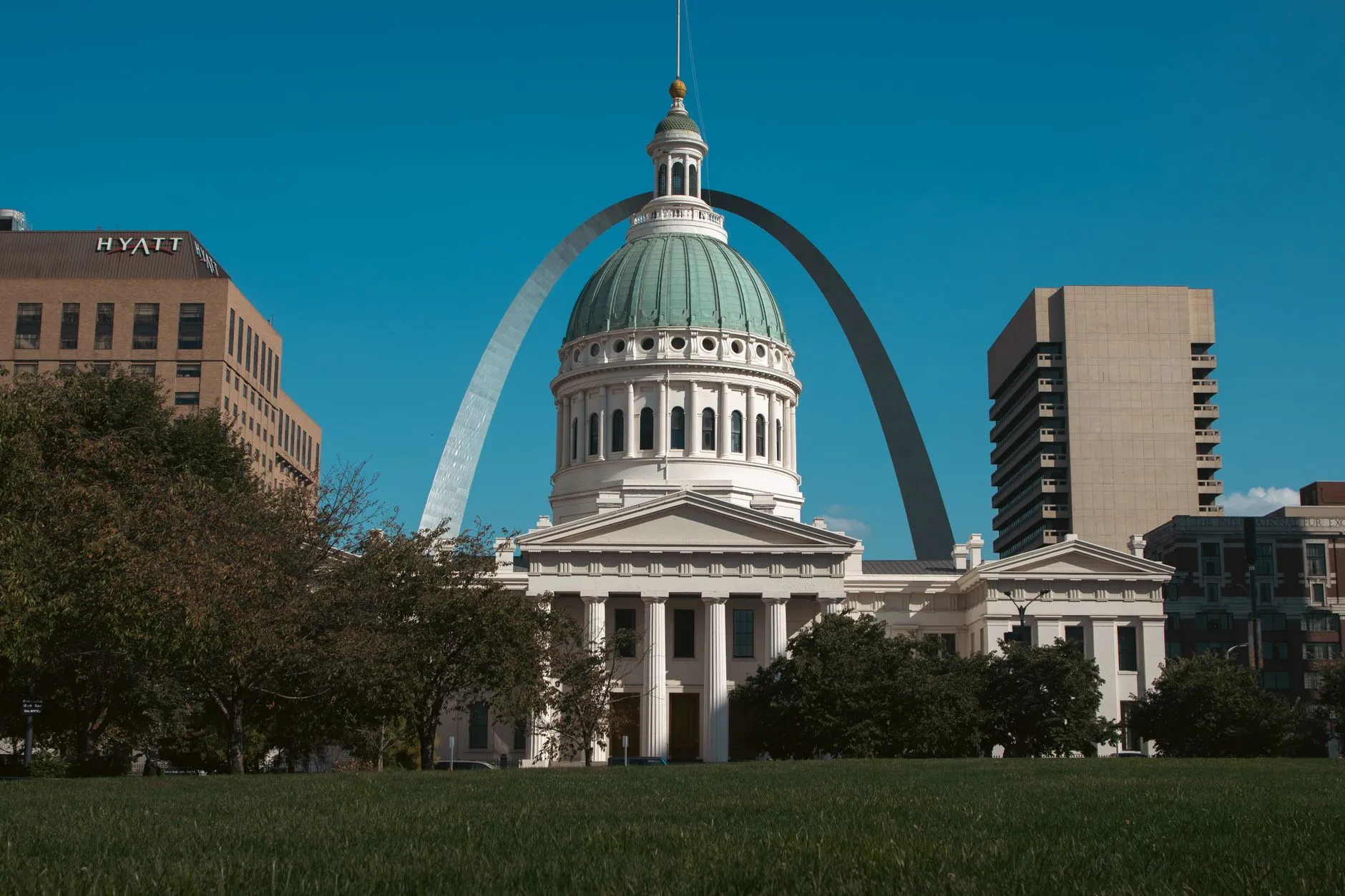 The green dome of the Old Courthouse in St. Louis, framed by the Gateway Arch rising behind it against a clear sky.